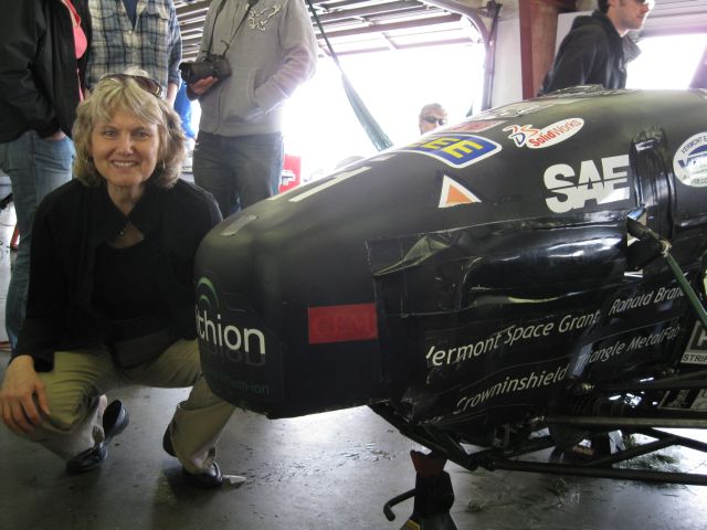 Elithion's Ann Colcord by nose of car, with Elithion decal